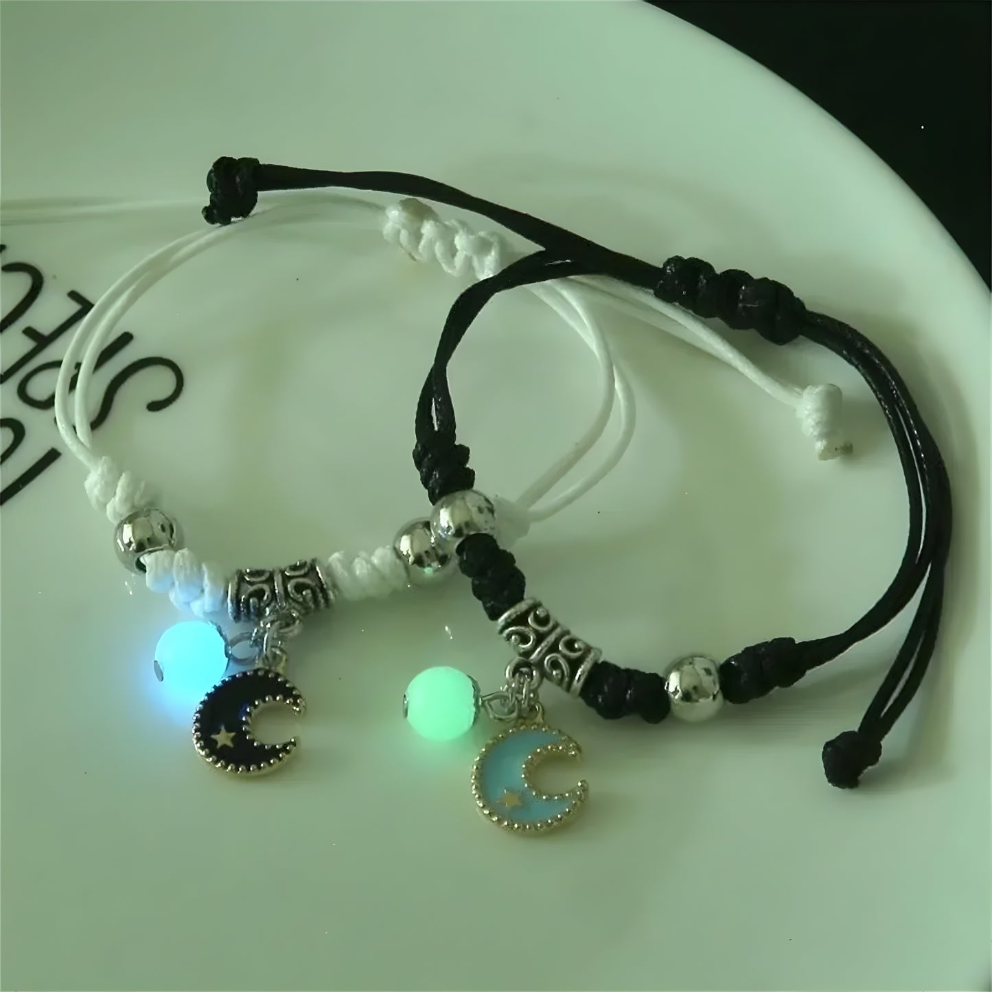 Two couple bracelets with luminous beads. One has a star-shaped bead, and the other has a moon-shaped bead, both with silver accents and black strings.