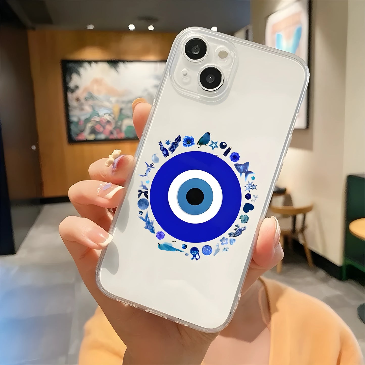 A clear phone case with a blue evil eye design and text reading 'GOOD VIBES' held in a person's hand.