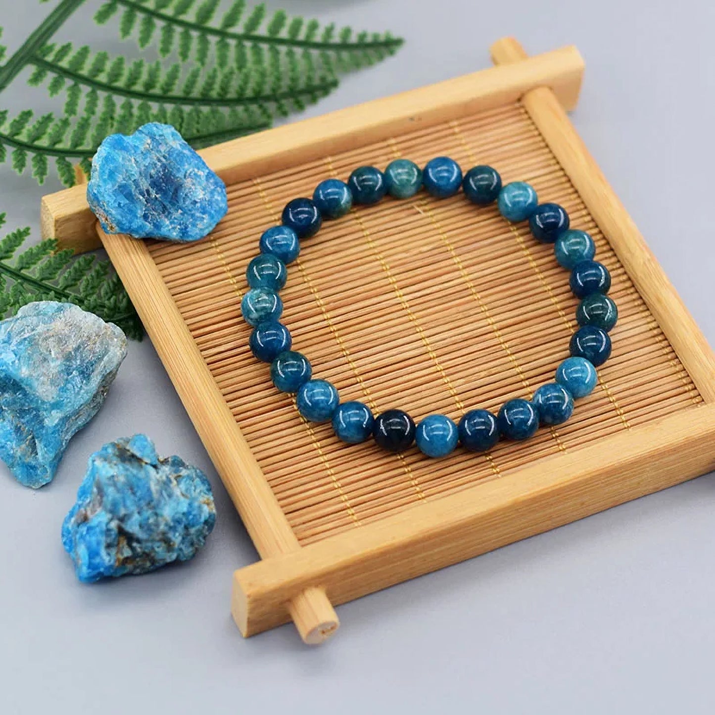 Blue beaded bracelet on a wooden tray with blue stones and green leaves in the background