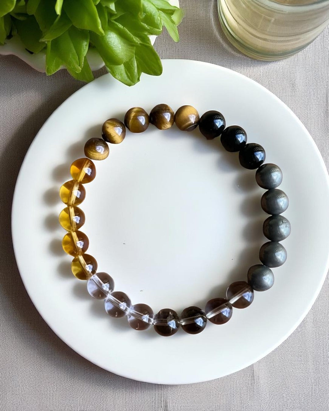 Beaded bracelet on a white plate with a plant and glass in the background