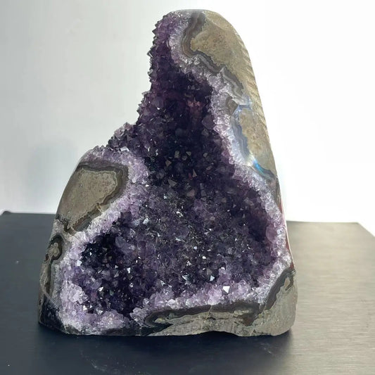 “High-resolution natural amethyst geode crystal cluster with deep purple crystal points and raw stone edges, displayed against a white and black background.”

